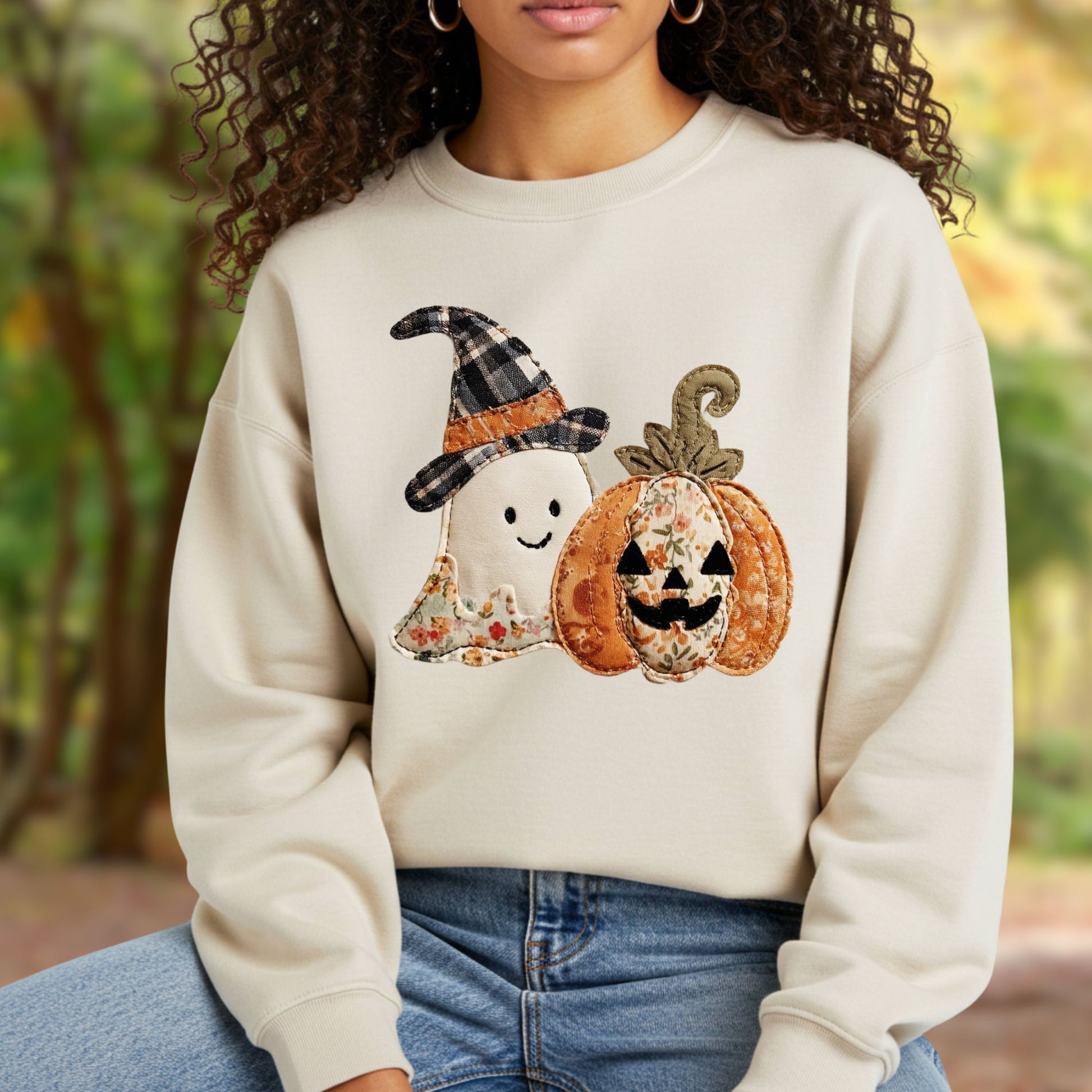 Cream sweatshirt with faux patchwork ghost in witch hat and jack-o-lantern, worn by a person outdoors.