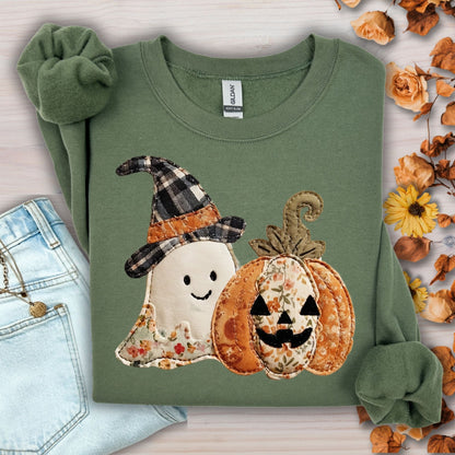 Military green Gildan sweatshirt with a faux patchwork ghost and jack-o-lantern print, beside jeans and fall leaves.