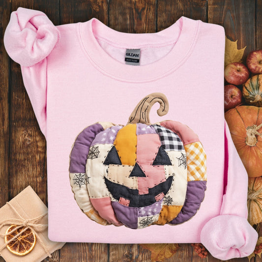 Light pink Gildan sweatshirt with a quilted, faux patchwork jack-o-lantern in pink, purple, and orange tones.
