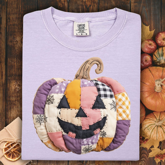 Orchid Comfort Colors tee with a whimsical faux patchwork jack-o'-lantern in pink, purple, and orange tones.