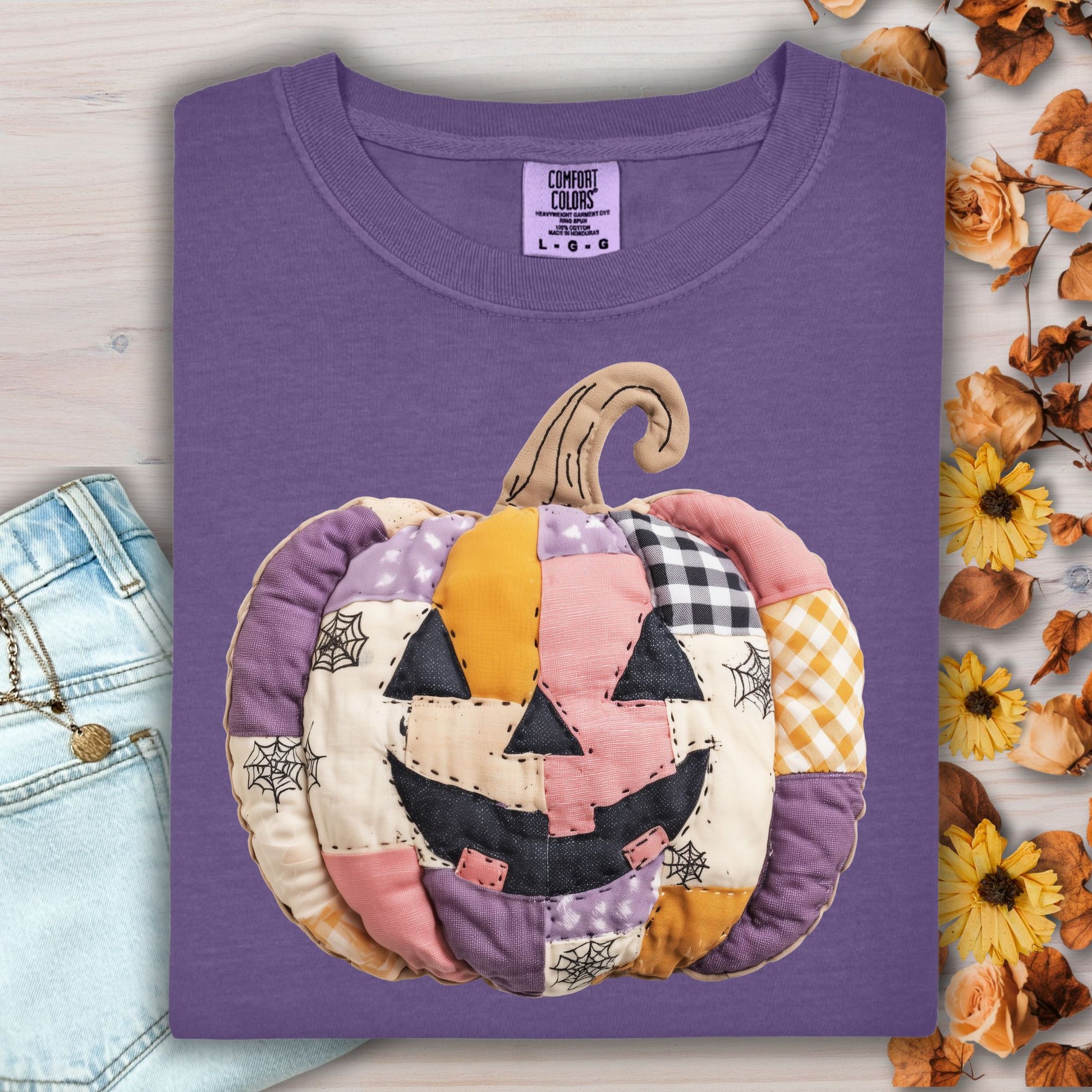 Grape Comfort Colors tee with a whimsical faux patchwork jack-o'-lantern in pink, purple, and orange tones.