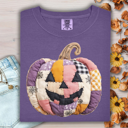 Grape Comfort Colors tee with a whimsical faux patchwork jack-o'-lantern in pink, purple, and orange tones.