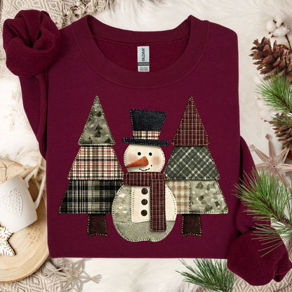 Maroon Gildan sweatshirt with a faux patchwork snowman and evergreen trees in earth tones.