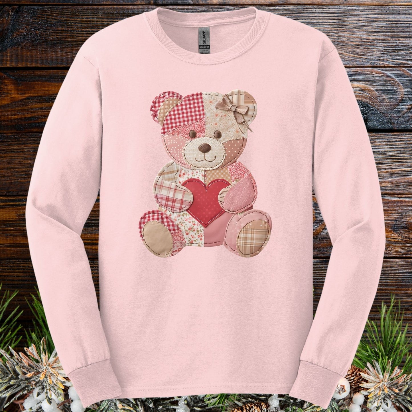 Light pink long-sleeve tee with a faux patchwork teddy bear holding a red heart.