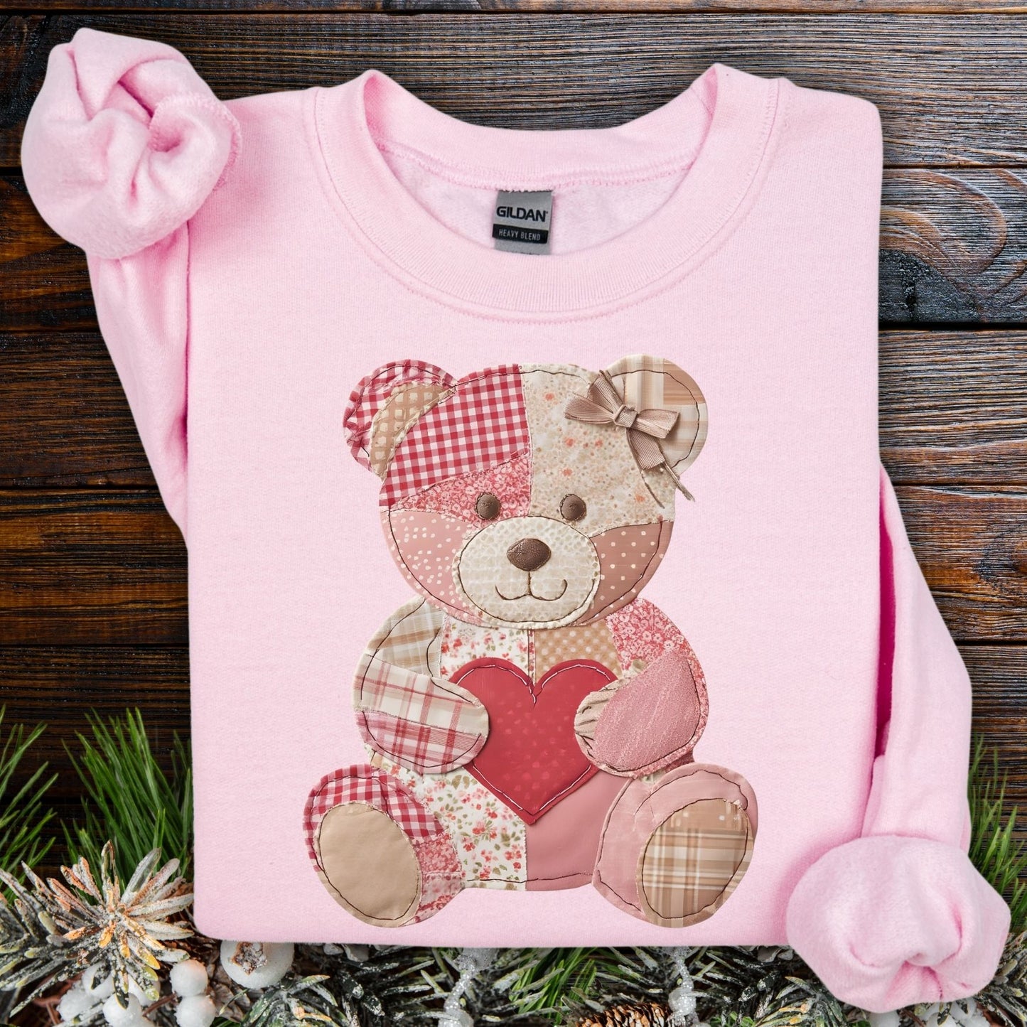 Light pink crewneck sweatshirt with a faux patchwork teddy bear holding a red heart.
