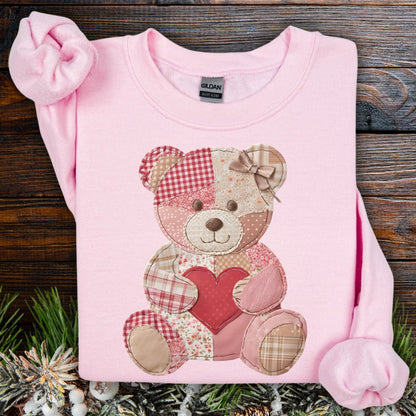 Light pink crewneck sweatshirt with a faux patchwork teddy bear holding a red heart.