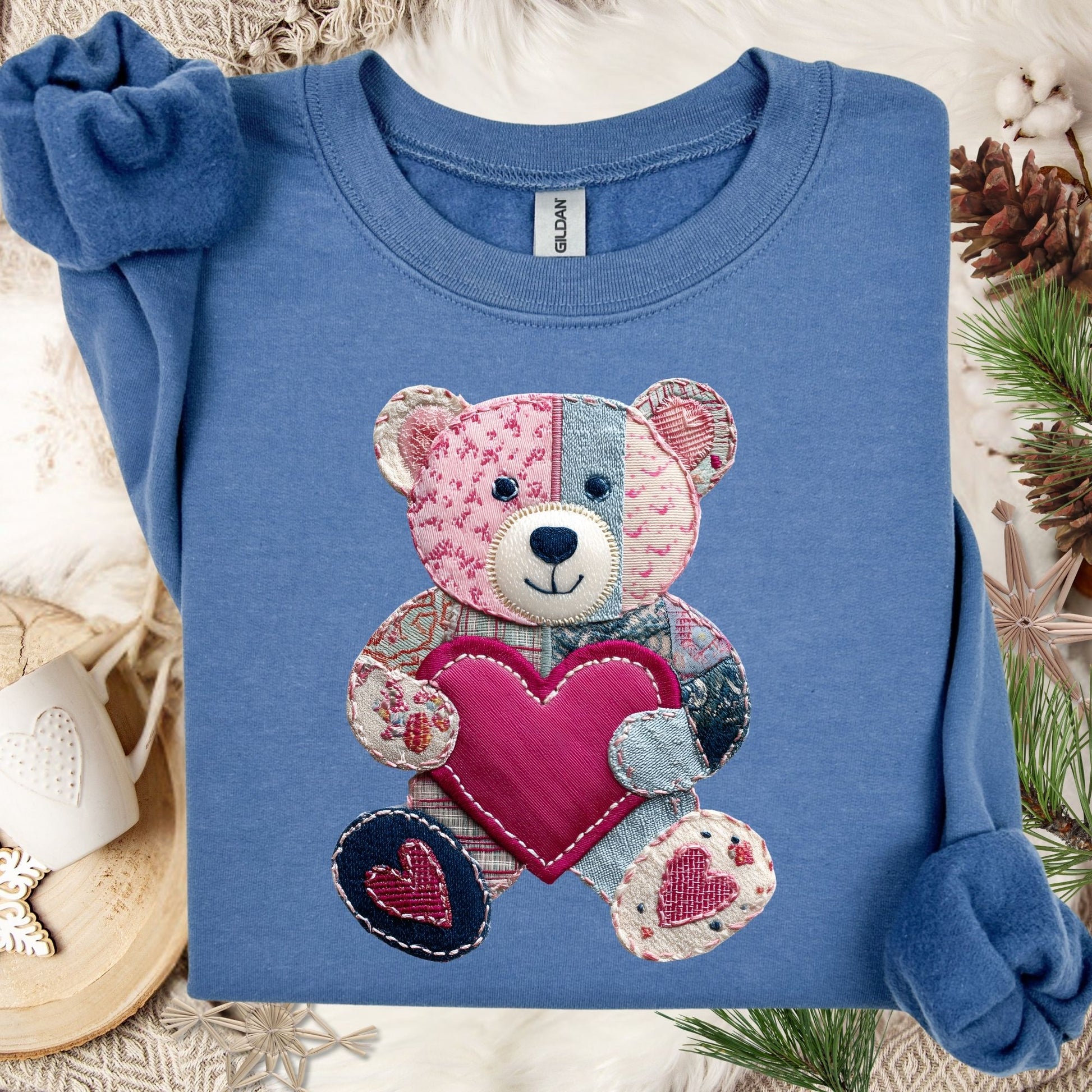 Indigo Blue Faux Patchwork Valentine's Teddy Bear Sweatshirt with a pink heart, folded on a cozy background.