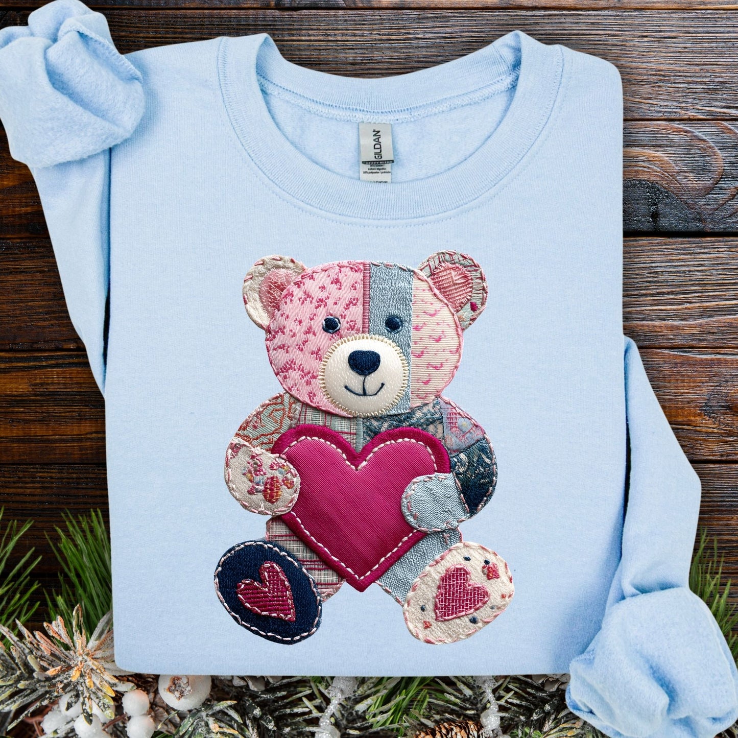 Light blue S sweatshirt with a printed faux patchwork teddy bear holding a pink heart.