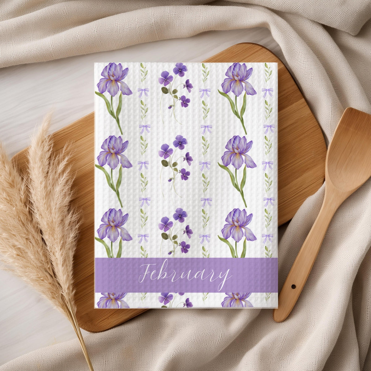 February birth month flower tea towel with purple iris and violet design on a wooden board.