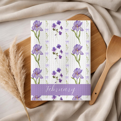 February birth month flower tea towel with purple iris and violet design on a wooden board.