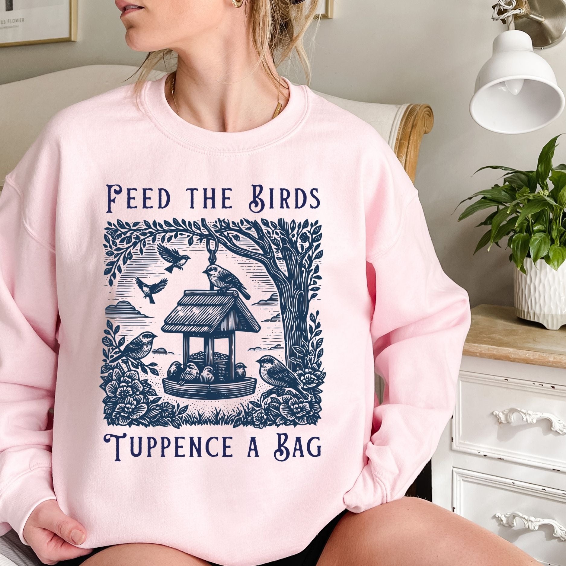 Pink crewneck sweatshirt with "Feed the Birds, Tuppence a Bag" text and a vintage bird feeder illustration.