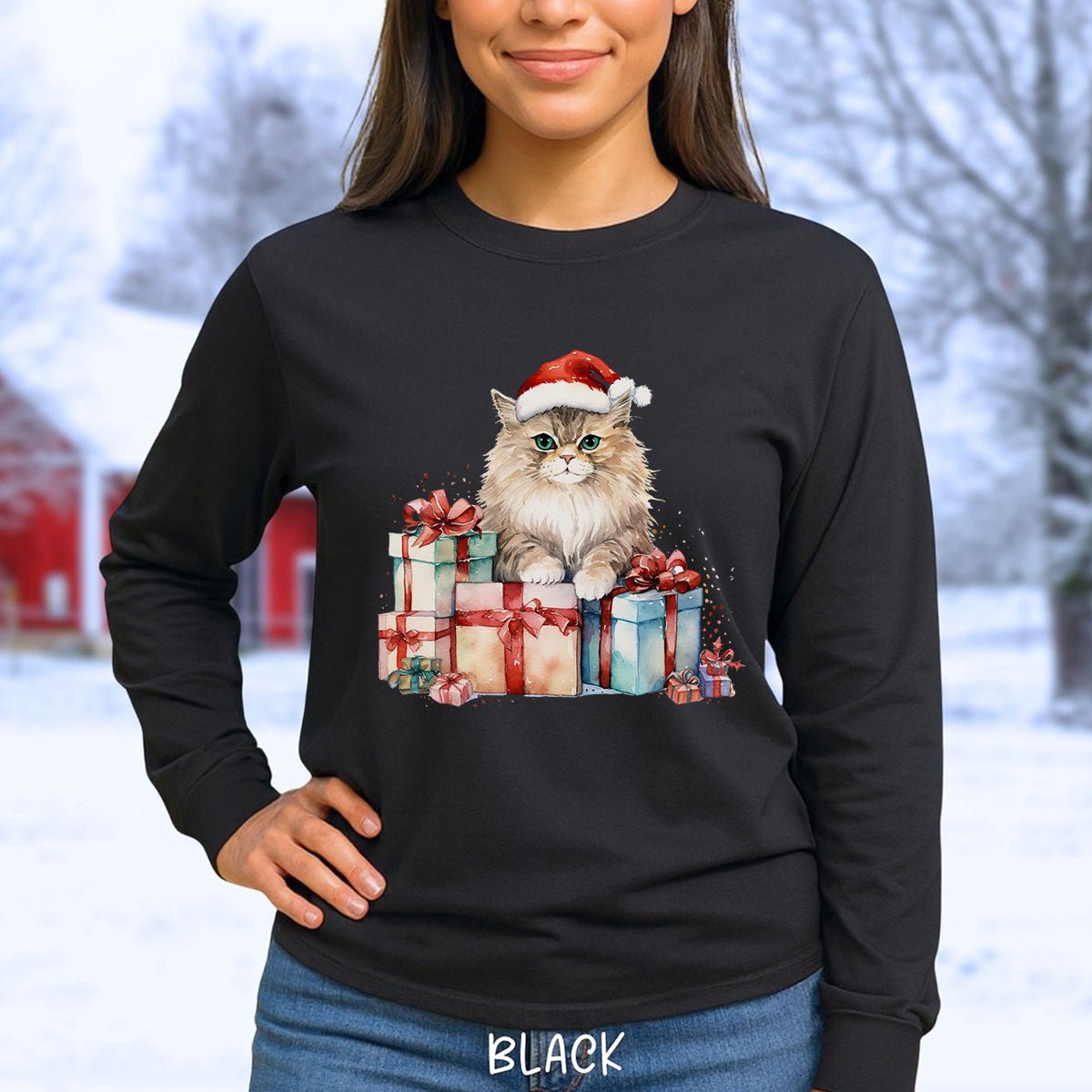 A woman wearing a black long-sleeve t-shirt with a graphic of a fluffy cat wearing a Santa hat and sitting on wrapped Christmas presents. The background is a blurred snowy outdoor scene.