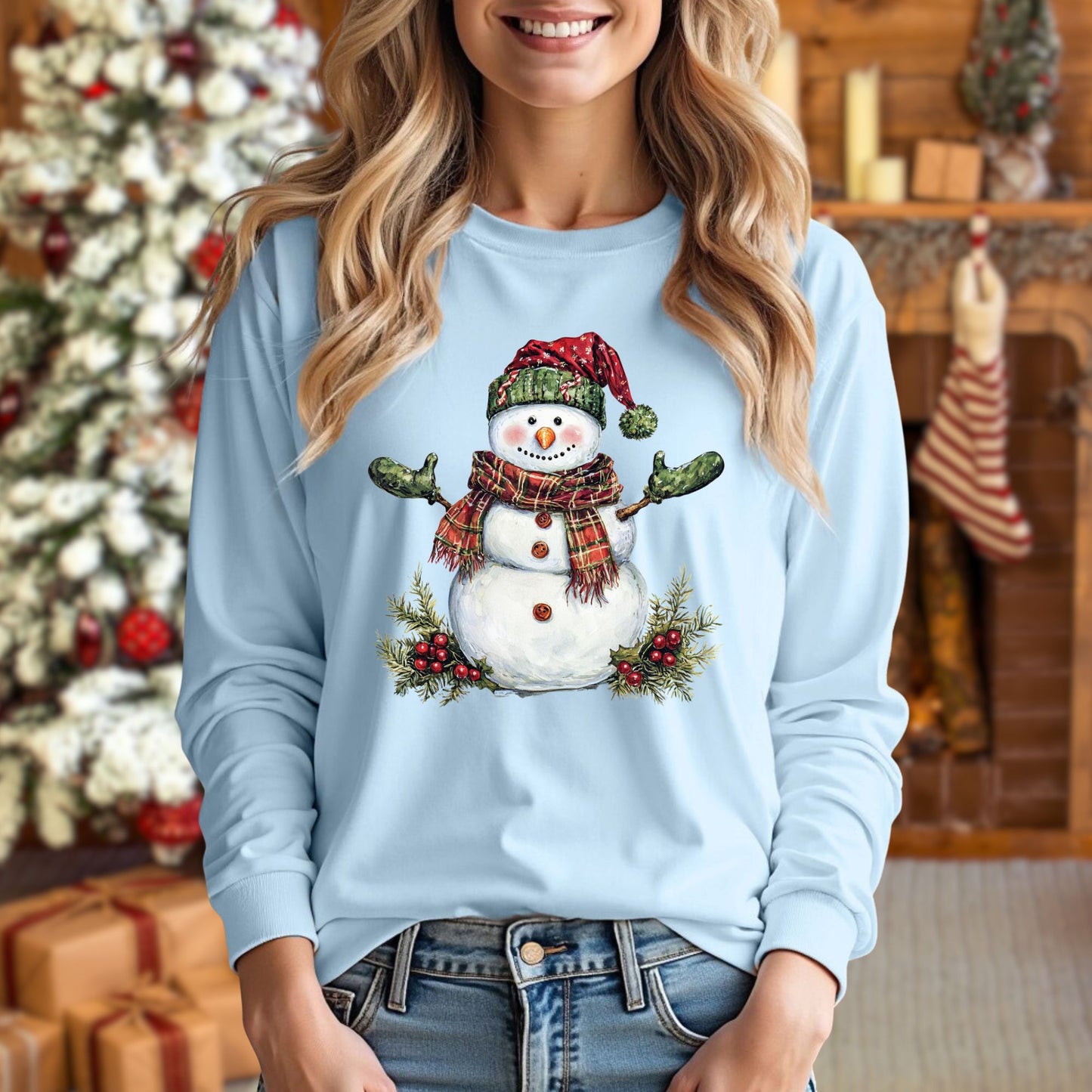 Woman wearing a light blue long sleeve tee with a watercolor snowman in a plaid hat and scarf.