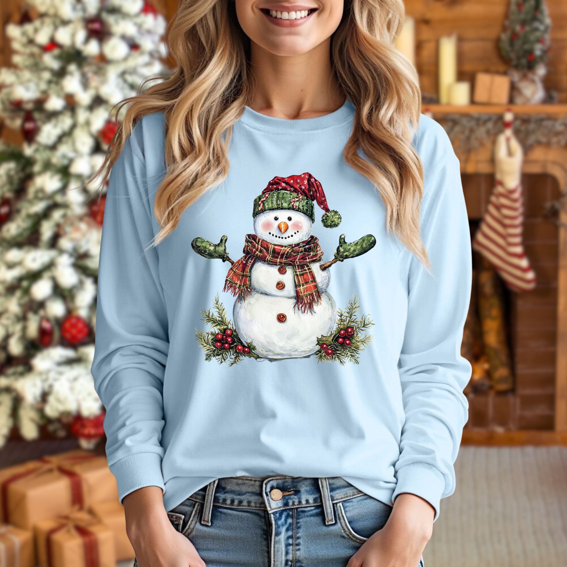 Woman wearing a light blue long sleeve tee with a watercolor snowman in a plaid hat and scarf.