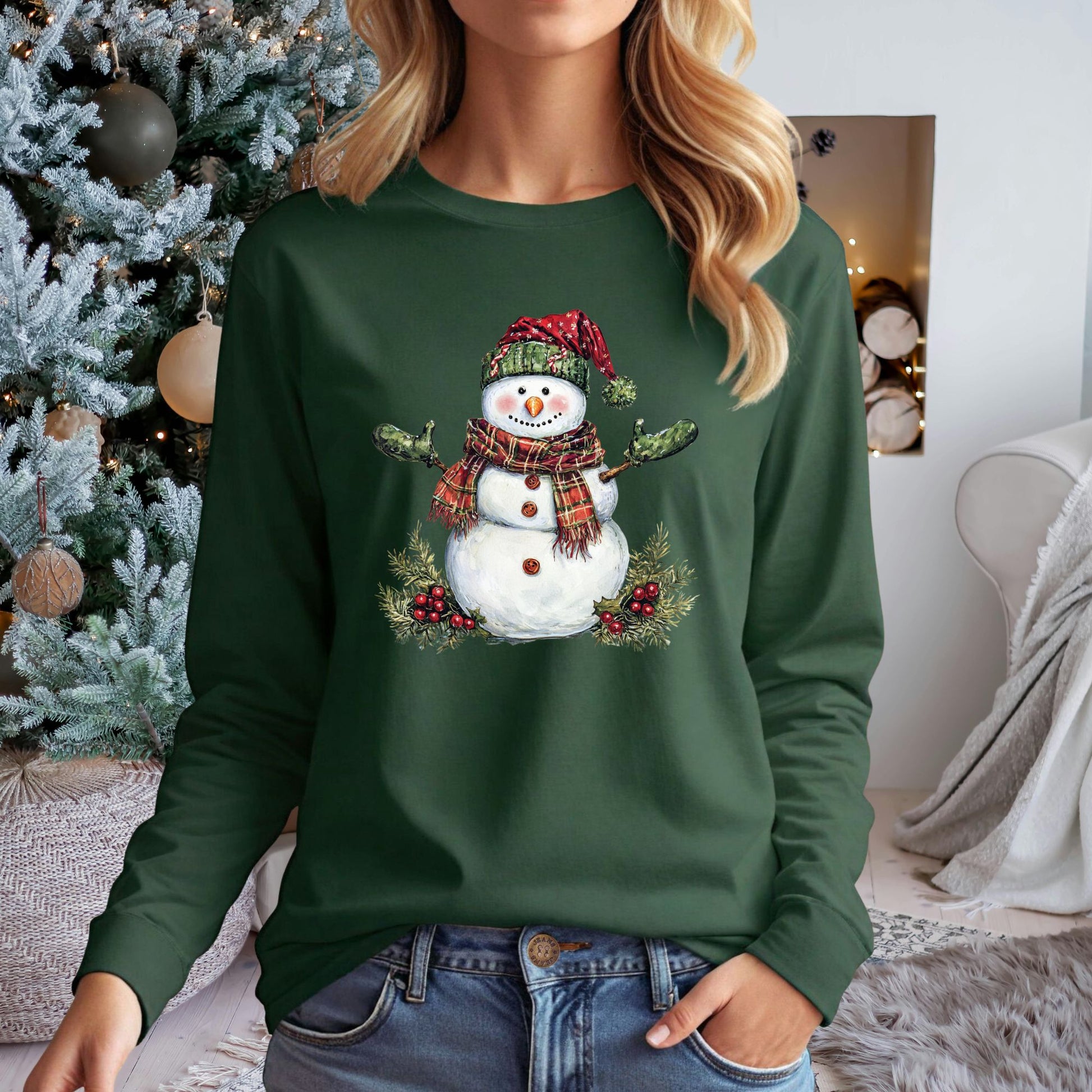 Green long-sleeve tee with a watercolor snowman wearing a plaid hat, green gloves, and scarf, surrounded by holly.