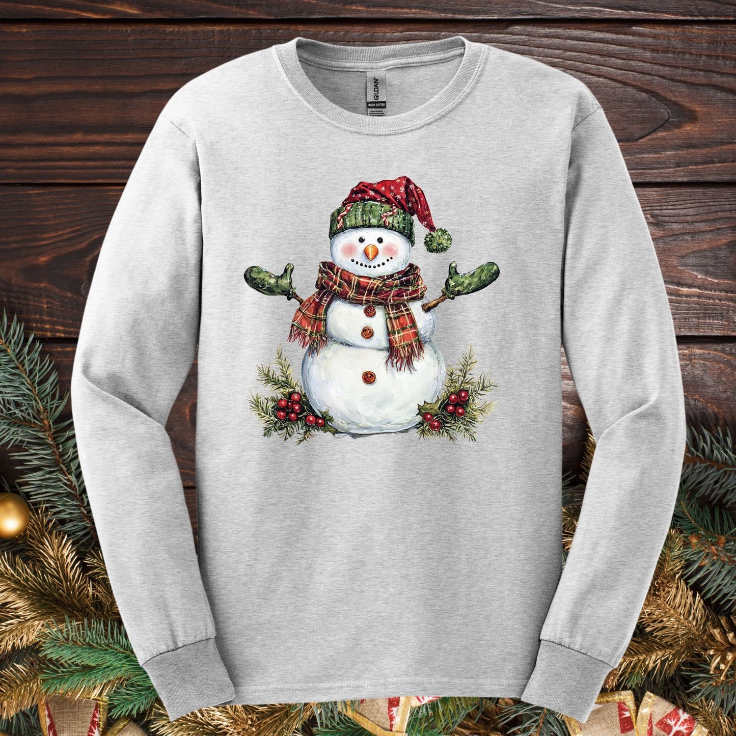Ash long sleeve tee with a watercolor snowman in a plaid hat, scarf, and green gloves.