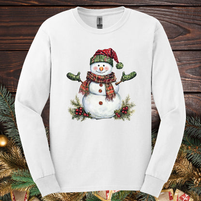 White long sleeve tee with a watercolor snowman in a plaid hat, green gloves, and holly.
