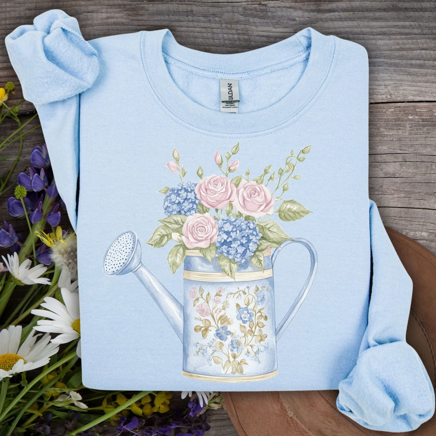 Light blue crewneck sweatshirt with a watercolor watering can blooming with pastel roses and hydrangeas.