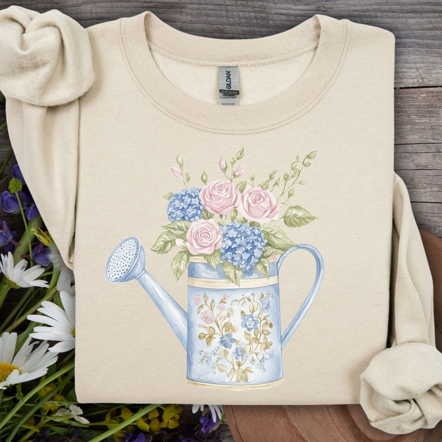 Sand crewneck sweatshirt with a watercolor watering can design featuring pink roses and blue hydrangeas.