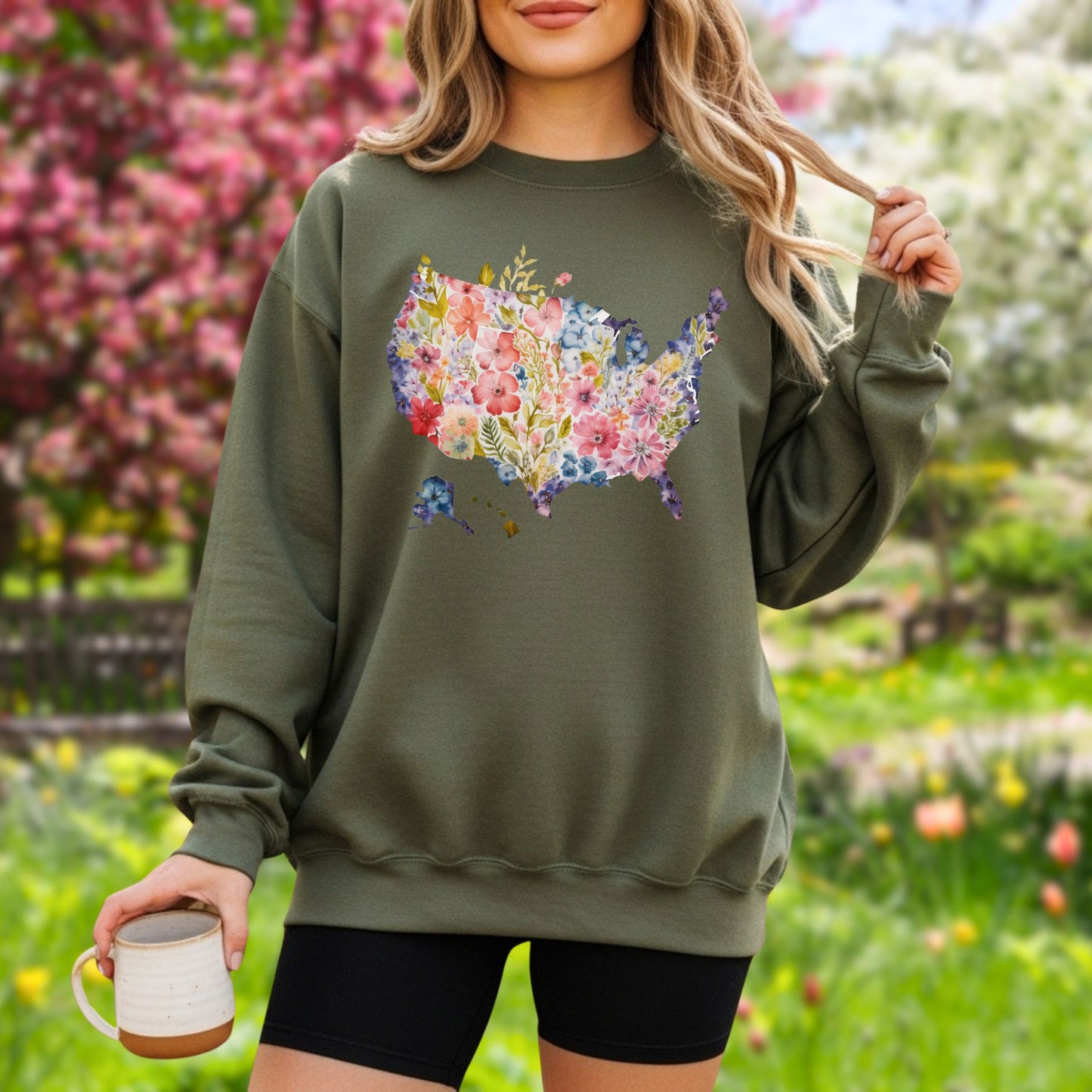 Olive green unisex sweatshirt with a watercolor floral USA map design worn by a person outdoors.