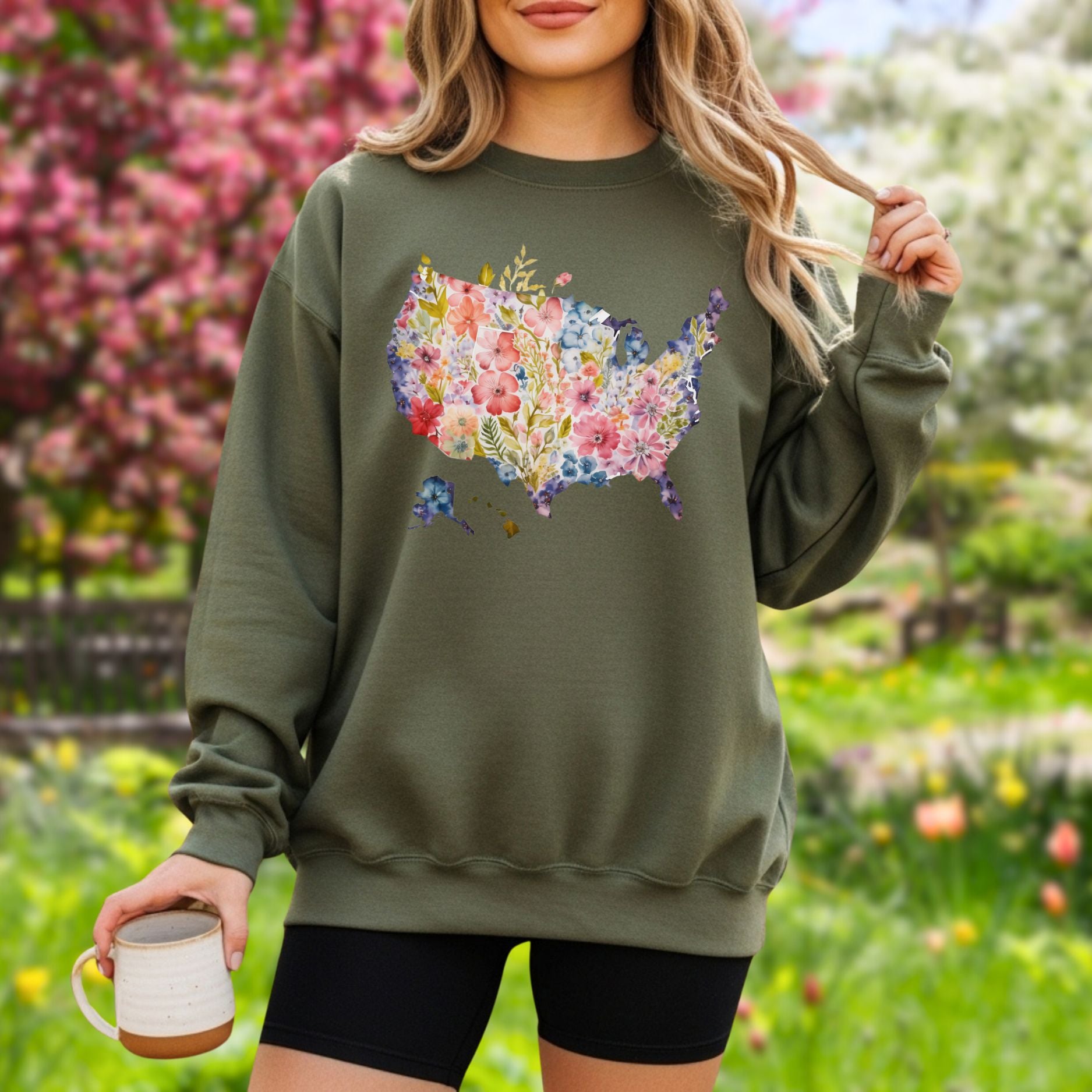 Olive green unisex sweatshirt with a watercolor floral USA map design worn by a person outdoors.
