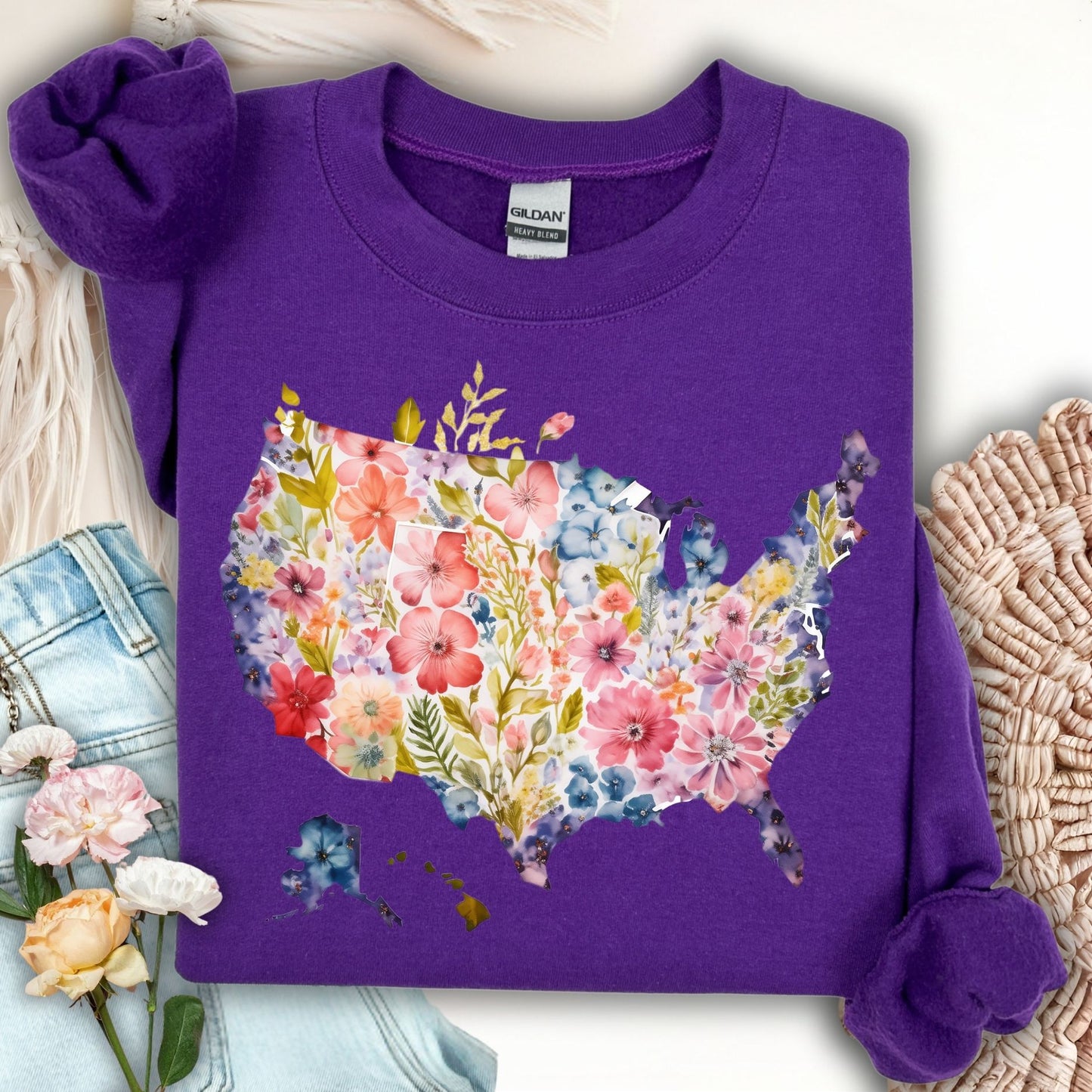 Purple Gildan sweatshirt with a watercolor floral USA map design, shown with jeans and flowers.