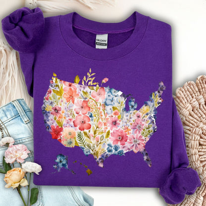 Purple Gildan sweatshirt with a watercolor floral USA map design, shown with jeans and flowers.