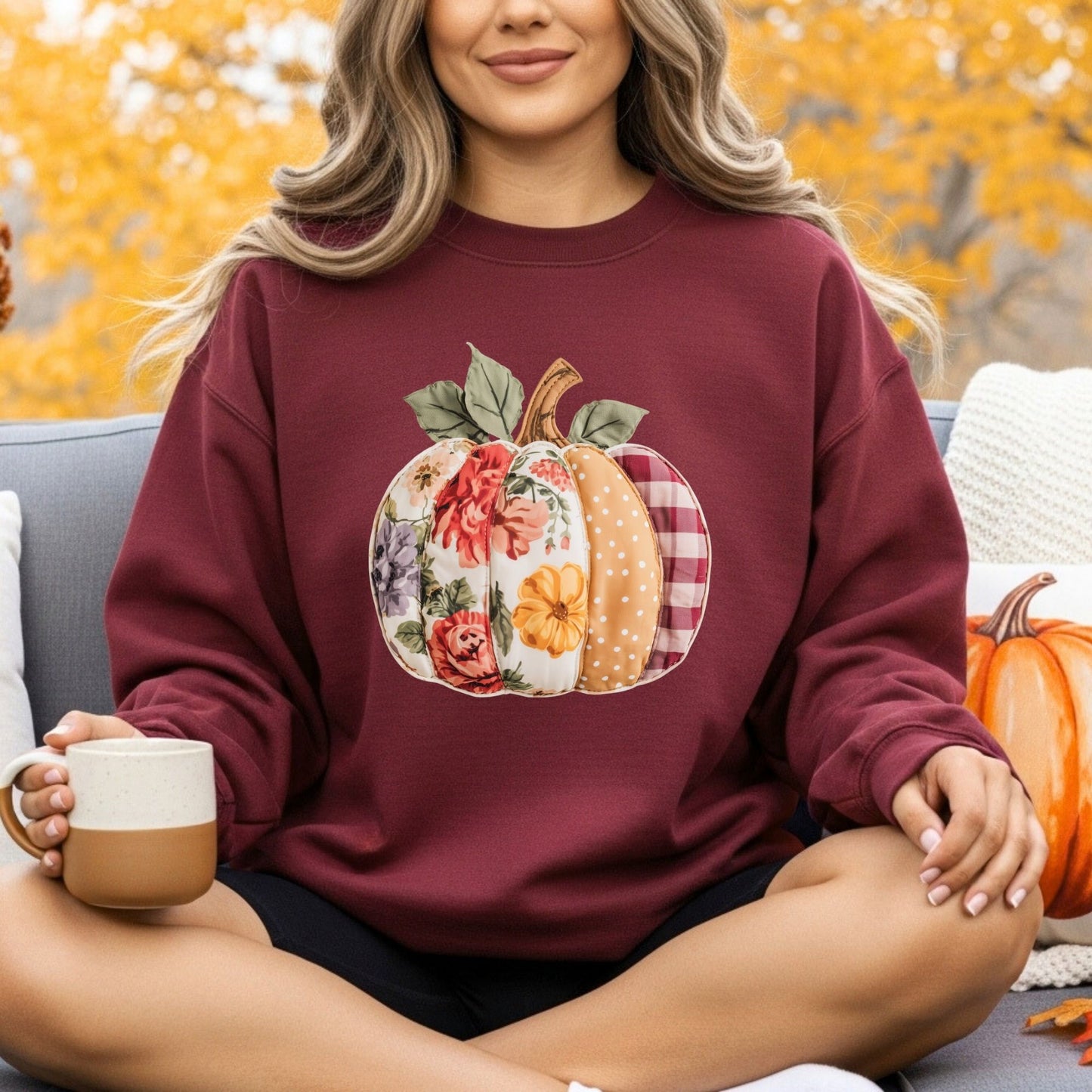 Woman in a maroon crewneck sweatshirt with a floral, gingham, and polka dot patchwork pumpkin design.