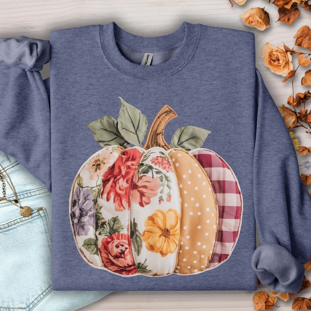 Heathered blue crewneck sweatshirt with a faux patchwork pumpkin design featuring floral, gingham, and polka dot patterns.