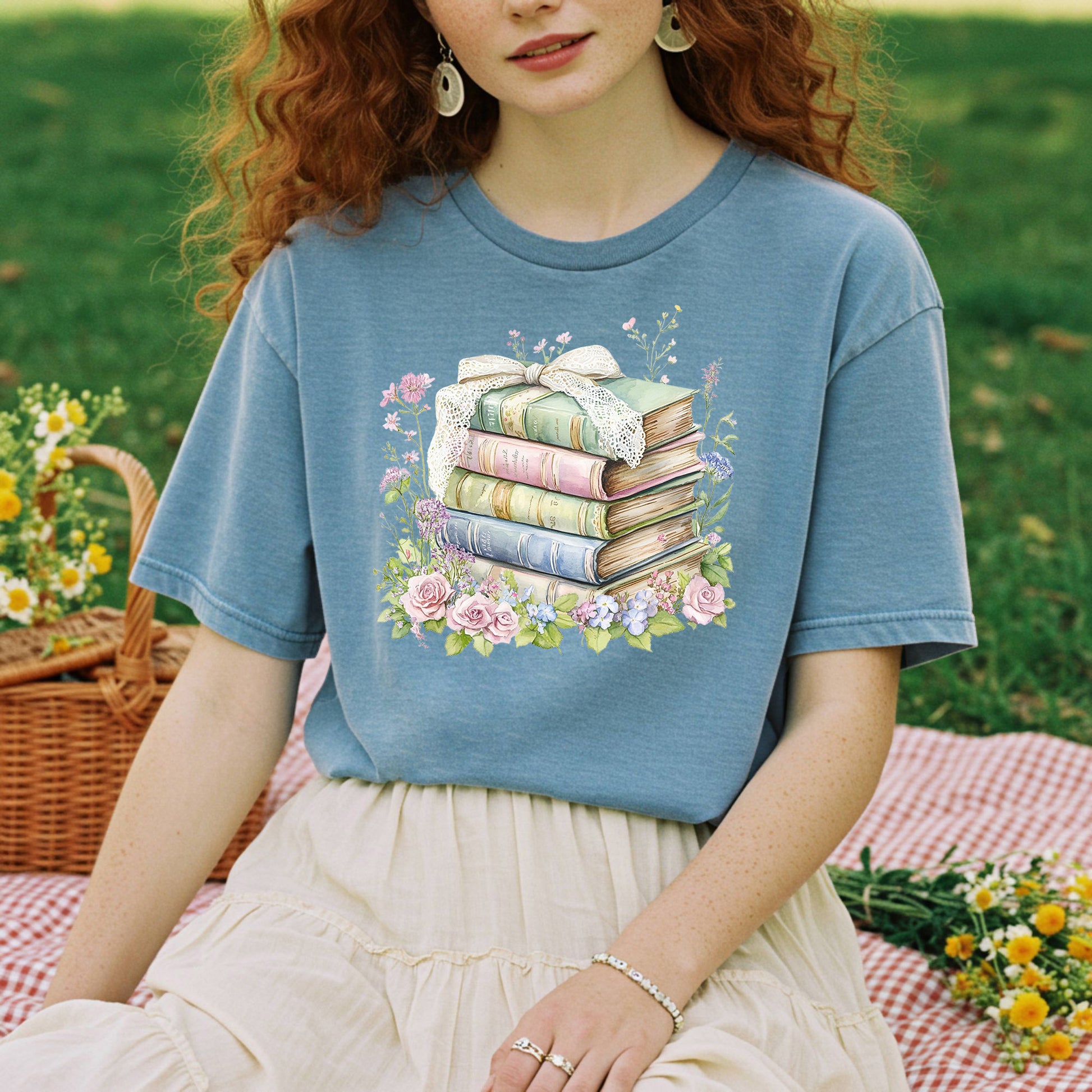 Woman in a blue t-shirt with a watercolor stack of vintage books and floral design.