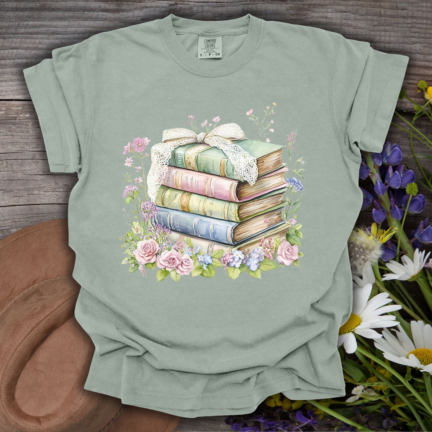 Bay S t-shirt with a watercolor stack of vintage books, lace ribbon, and pink, blue, and purple flowers.