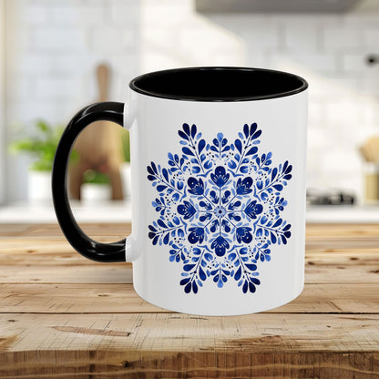 White ceramic mug with a black interior and handle, featuring a detailed blue floral snowflake mandala design.