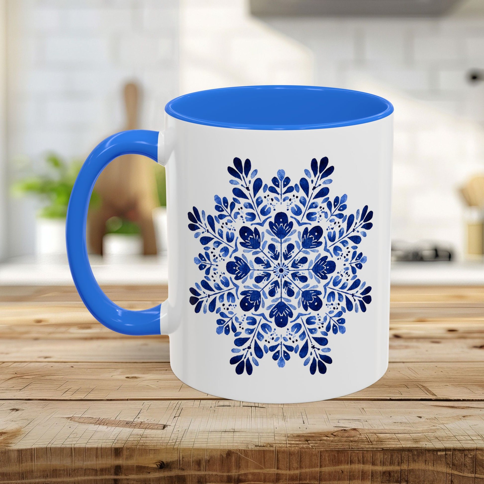 White ceramic mug with a blue interior and handle, featuring a detailed blue floral snowflake mandala design.