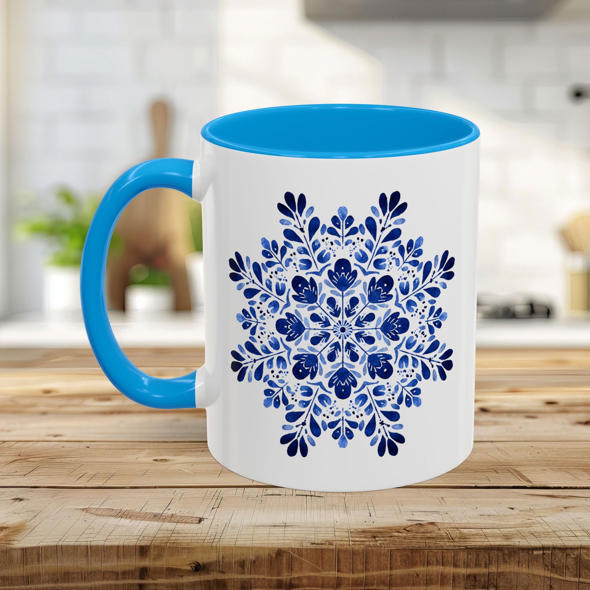 White ceramic mug with a bright blue interior and handle, featuring a detailed blue floral snowflake mandala.