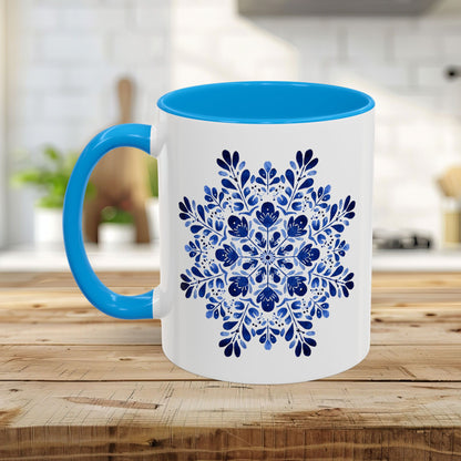 White ceramic mug with a bright blue interior and handle, featuring a detailed blue floral snowflake mandala.