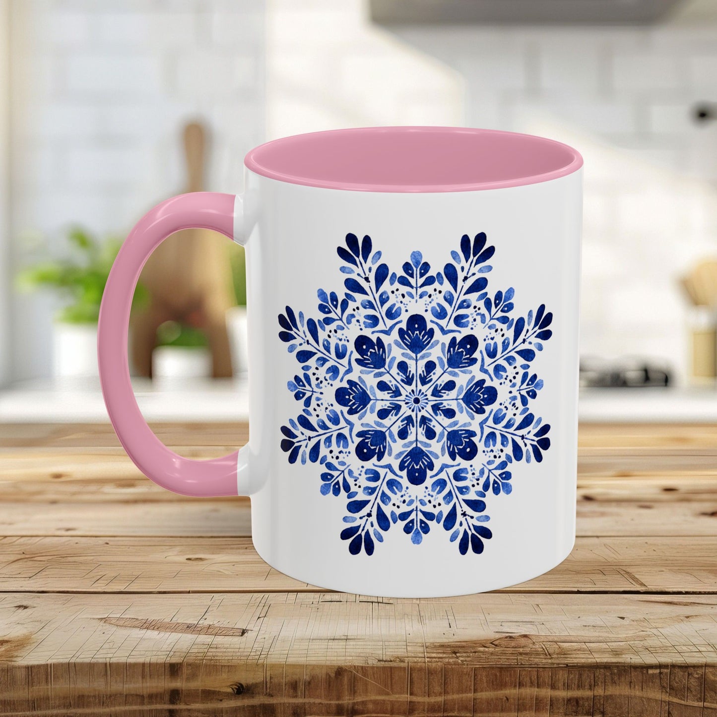 White ceramic mug with a pink interior and handle, featuring a blue floral snowflake mandala design.