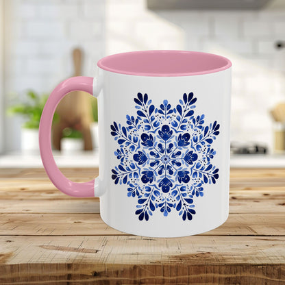 White ceramic mug with a pink interior and handle, featuring a blue floral snowflake mandala design.