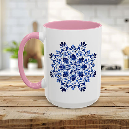 White ceramic mug with a pink interior and handle, featuring a blue floral snowflake mandala design.