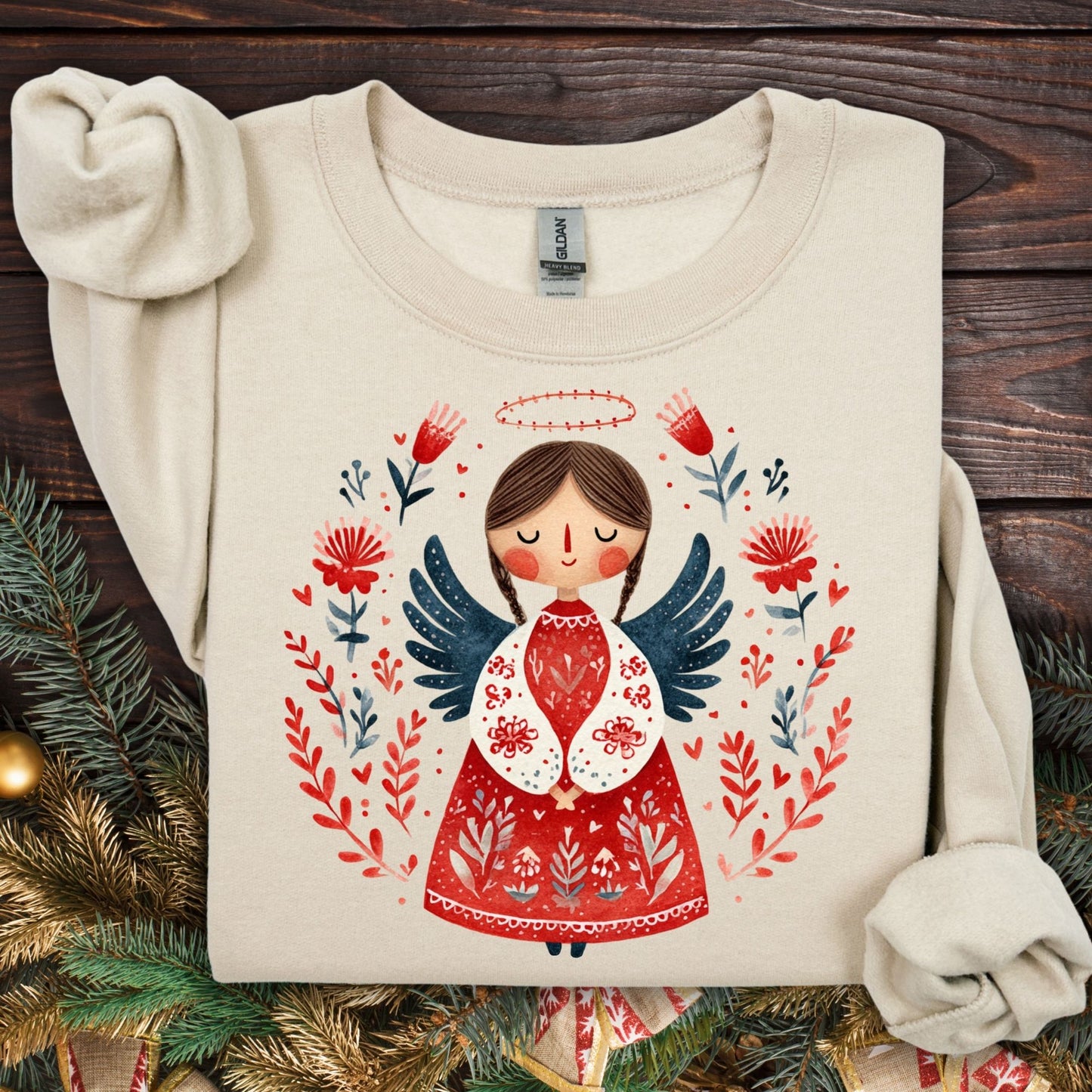 Sand Gildan sweatshirt with a folk art Christmas angel in red, green, and navy, surrounded by festive flora.