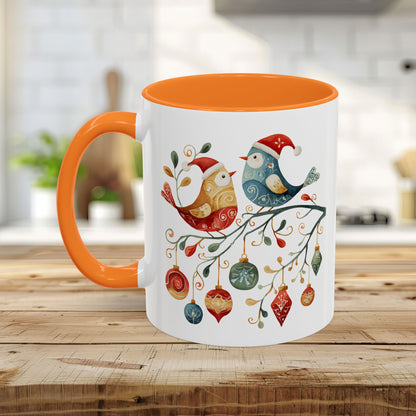 White ceramic mug with orange interior and handle, featuring two folk art Christmas birds on a branch with ornaments.