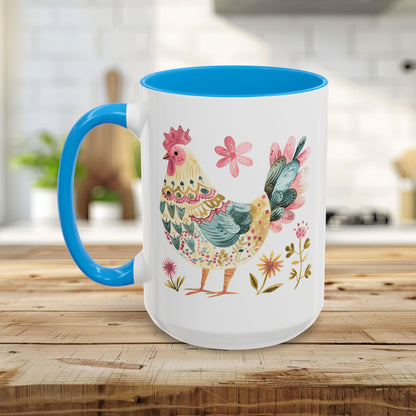 White ceramic mug with blue handle and interior, featuring a colorful folk art watercolor rooster and floral design.