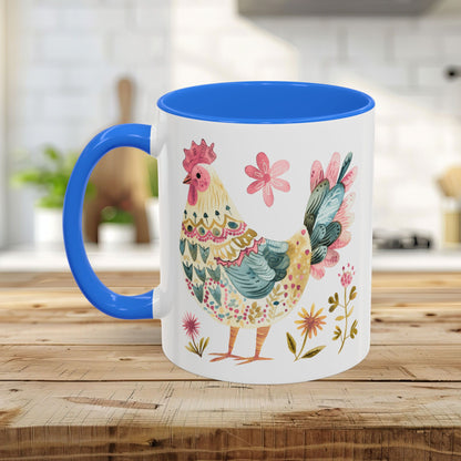 White ceramic mug with blue handle and interior, featuring a colorful folk art watercolor rooster and floral design.