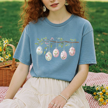Relaxed-fit, garment-dyed blue t-shirt with a folk art Easter egg branch design on a woman in a garden.