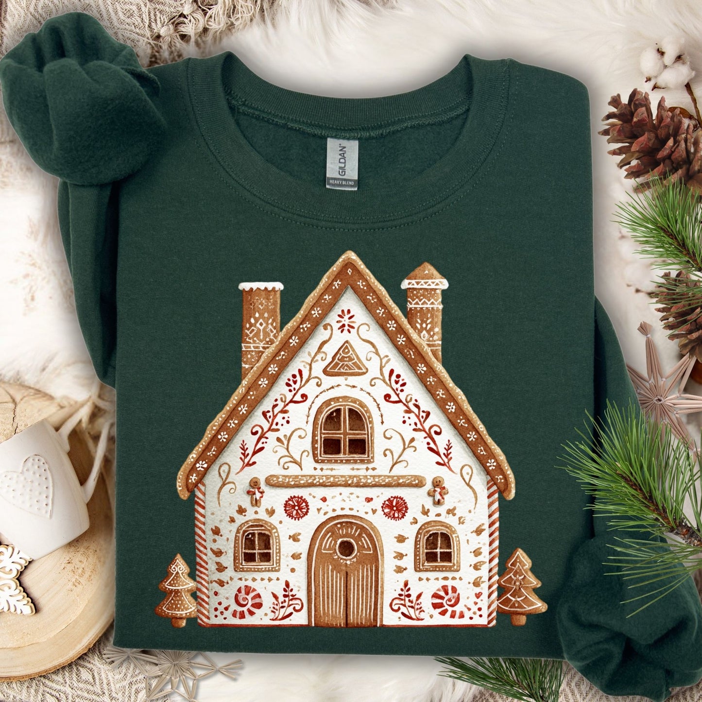 Forest Green Gildan sweatshirt with a folk art gingerbread house design, surrounded by pinecones and greenery.