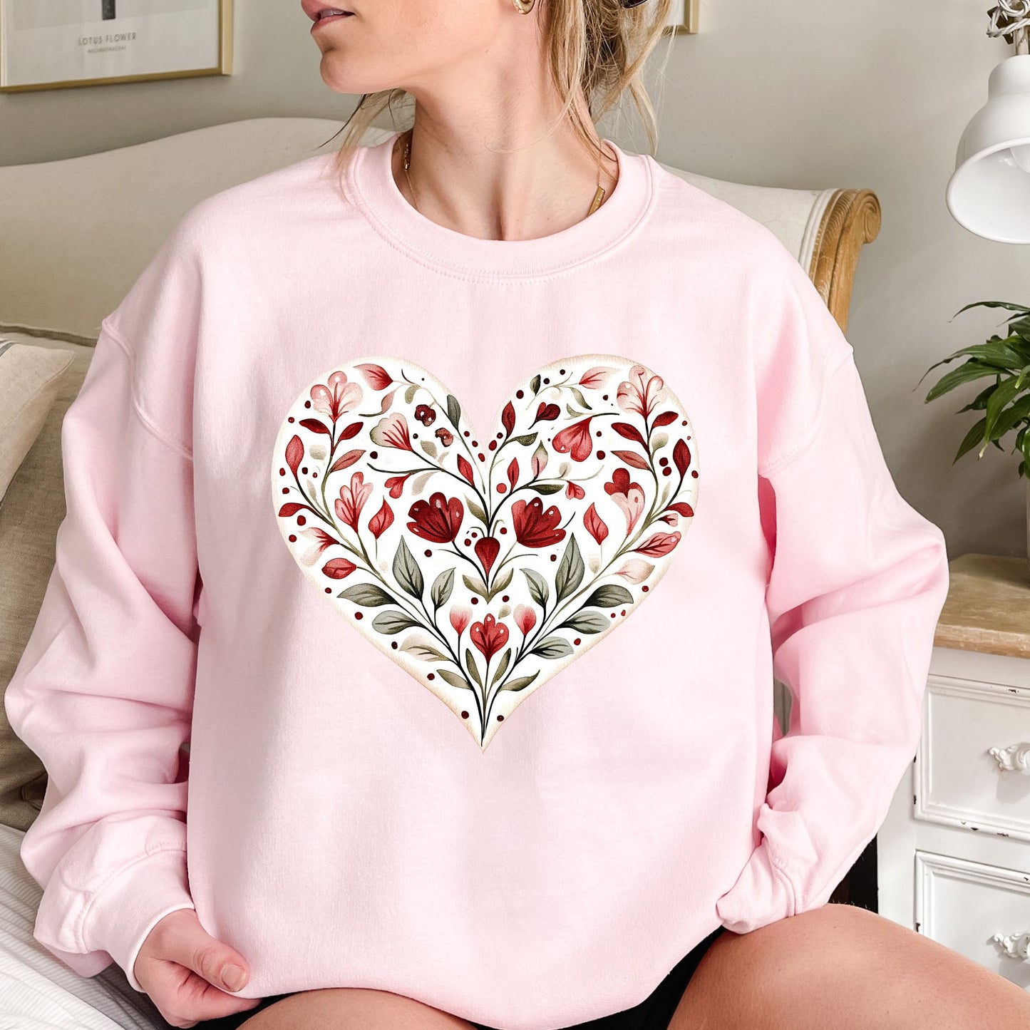Pink heavy blend sweatshirt with a folk art red floral heart design, worn by a woman.