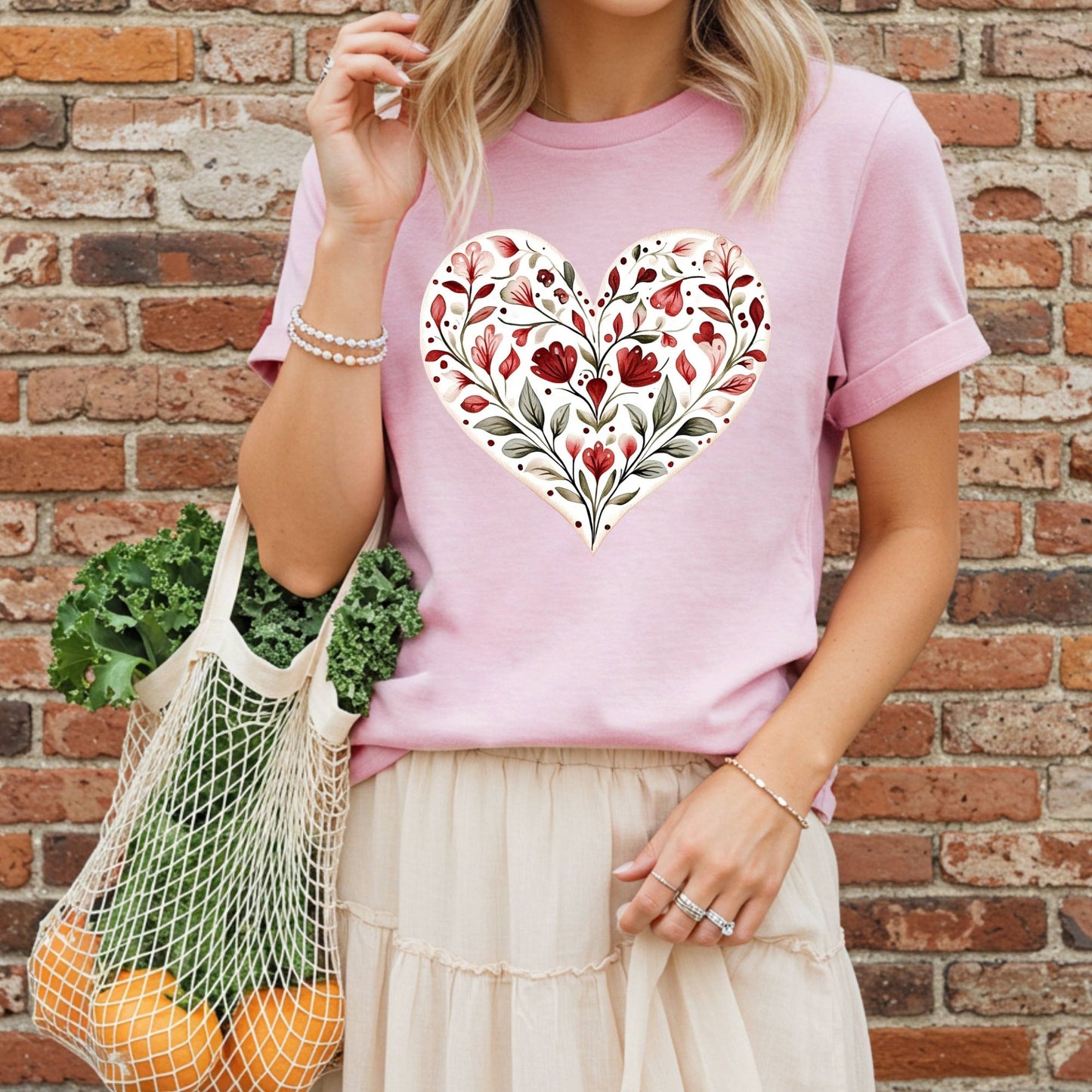 Relaxed-fit pink t-shirt with a painterly red floral heart design, worn by a woman holding a mesh bag.
