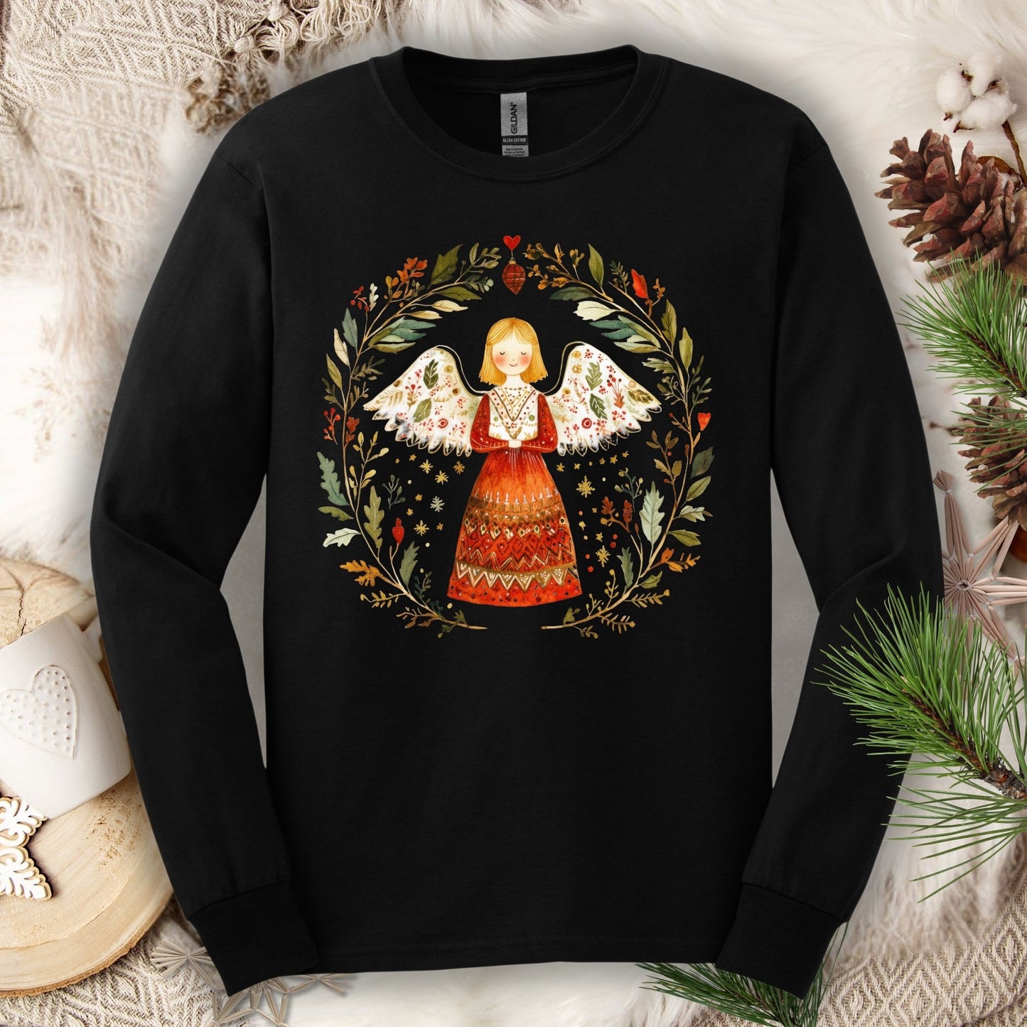 Black Gildan Softstyle long sleeve tee with a folk art winter angel in a red dress surrounded by a festive wreath.
