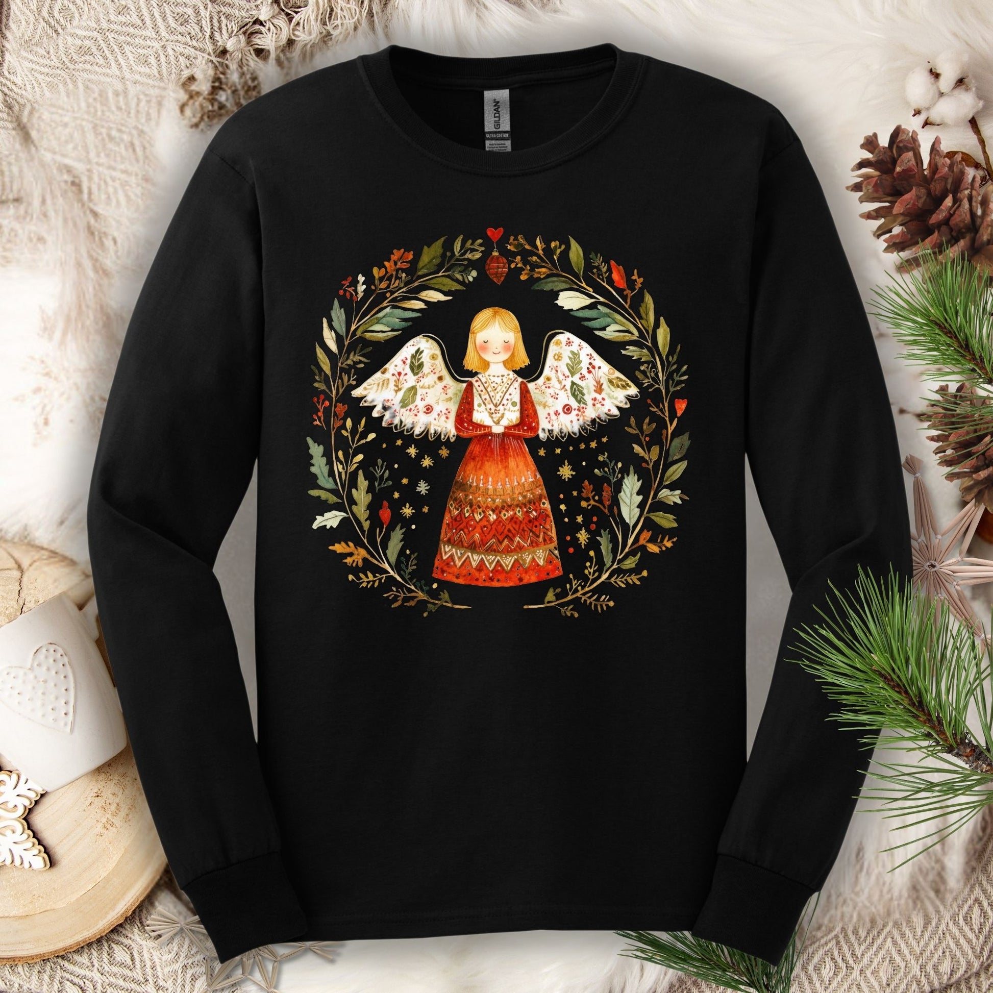 Black Gildan Softstyle long sleeve tee with a folk art winter angel in a red dress surrounded by a festive wreath.