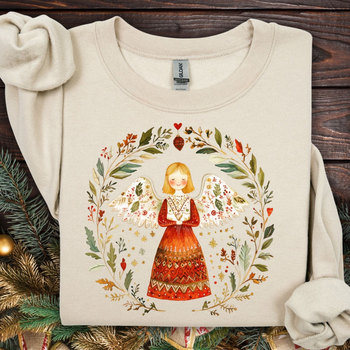 Sand S sweatshirt with a folk art angel in a winter wreath, featuring red, green, and golden hues.