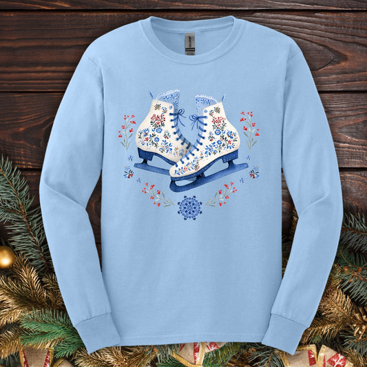 Light blue long sleeve tee with folk art winter ice skates in blues, reds, and whites, surrounded by florals.